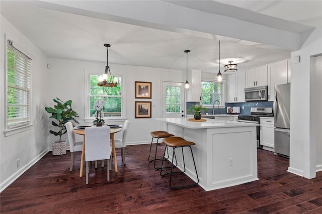 kitchen with a breakfast bar area, appliances with stainless steel finishes, backsplash, dark wood-style flooring, and white cabinetry