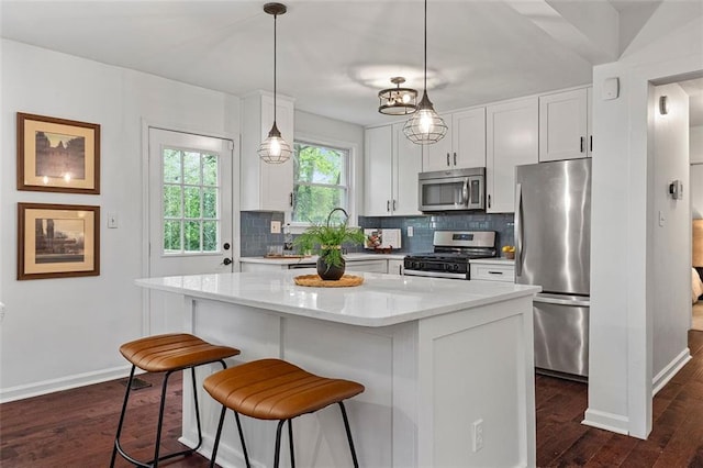 kitchen with tasteful backsplash, white cabinetry, appliances with stainless steel finishes, a kitchen bar, and dark wood-style floors