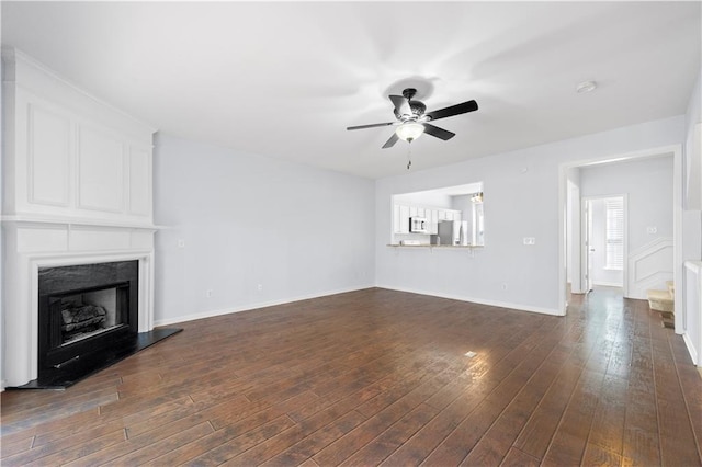 unfurnished living room with a fireplace, ceiling fan, dark wood-type flooring, stairs, and baseboards