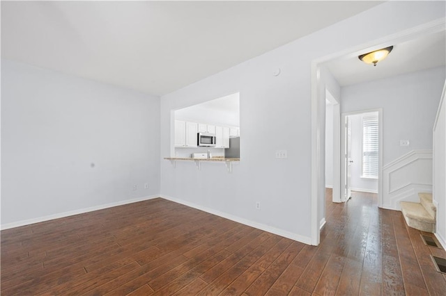 unfurnished living room featuring baseboards, dark wood finished floors, and stairs