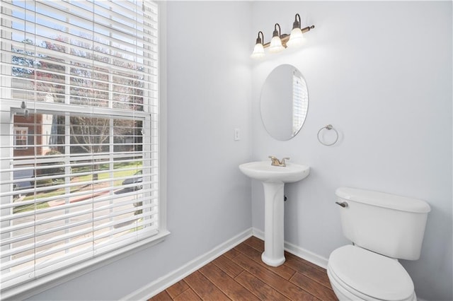 half bathroom with a wealth of natural light, wood finished floors, toilet, and baseboards