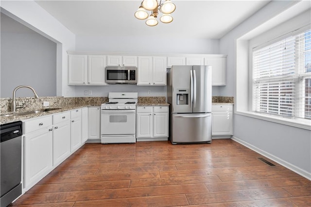 kitchen featuring stainless steel appliances, a sink, white cabinetry, visible vents, and a notable chandelier