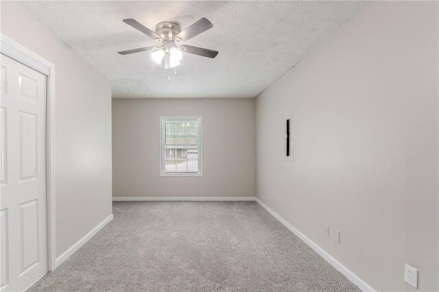 carpeted empty room with baseboards, ceiling fan, and a textured ceiling