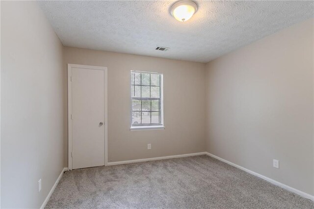 carpeted spare room with baseboards, a textured ceiling, and visible vents