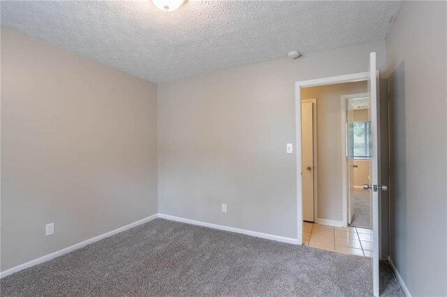 empty room with baseboards, a textured ceiling, and light colored carpet