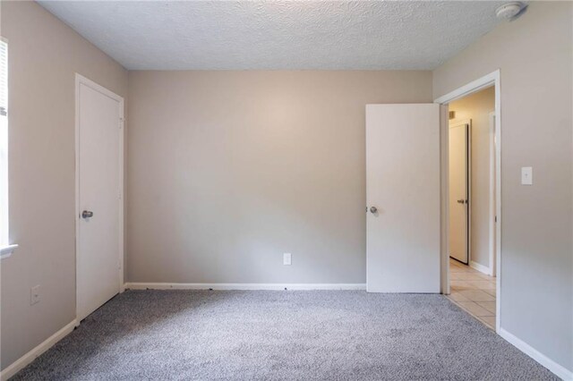 empty room featuring baseboards, a textured ceiling, and light colored carpet