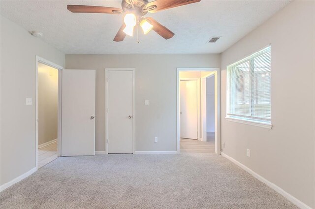 unfurnished bedroom featuring visible vents, light carpet, baseboards, a textured ceiling, and a ceiling fan