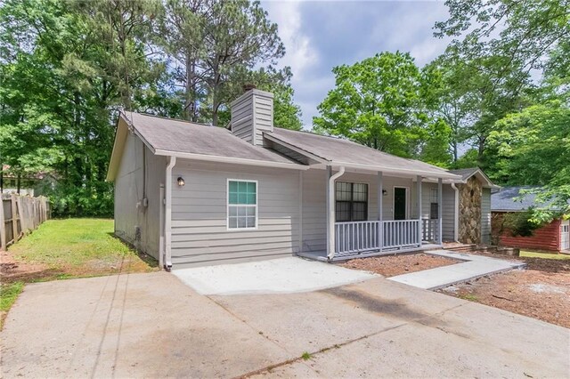 single story home featuring fence, covered porch, a chimney, and a front lawn