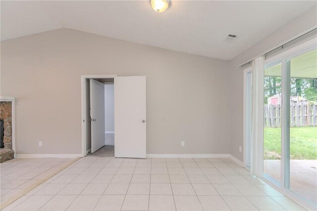 empty room featuring visible vents, a fireplace, baseboards, light tile patterned floors, and vaulted ceiling
