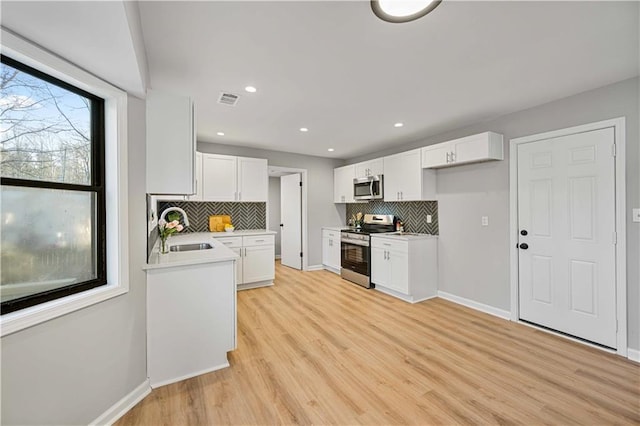 kitchen with visible vents, light wood finished floors, a sink, stainless steel appliances, and white cabinetry