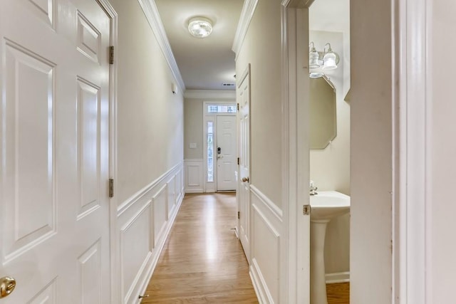 corridor featuring crown molding, wainscoting, light wood-type flooring, and a decorative wall