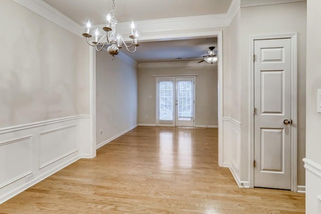 unfurnished dining area with ceiling fan with notable chandelier, wainscoting, light wood-style flooring, and crown molding