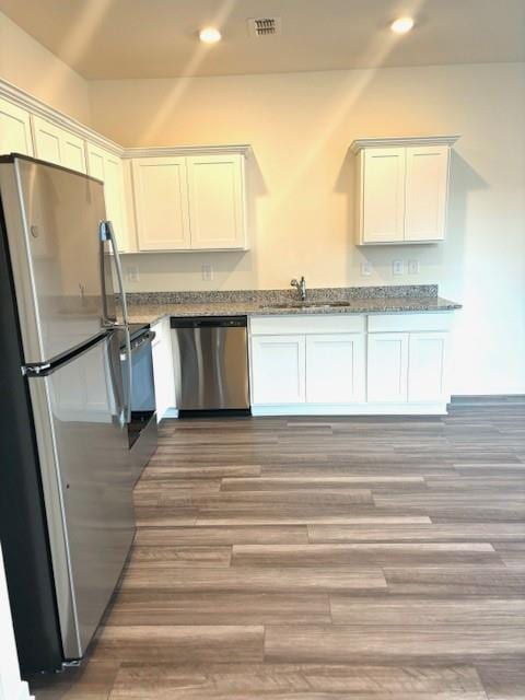 kitchen featuring sink, wood-type flooring, appliances with stainless steel finishes, stone counters, and white cabinets