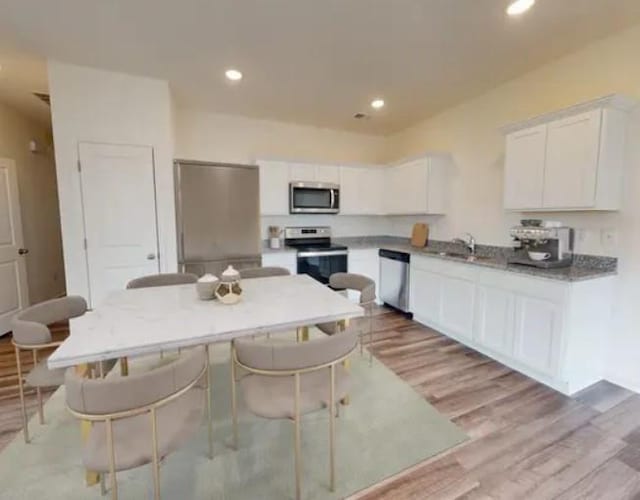 kitchen with appliances with stainless steel finishes, sink, white cabinets, light stone countertops, and light hardwood / wood-style flooring