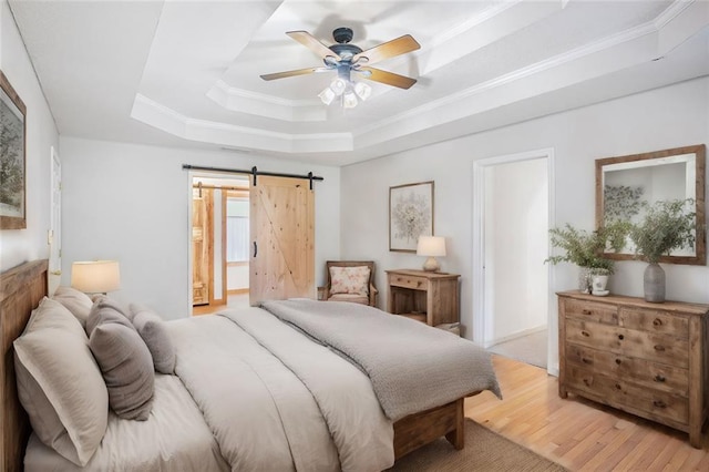 bedroom featuring ceiling fan, a raised ceiling, a barn door, crown molding, and light wood-type flooring