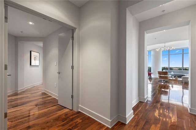 hallway featuring hardwood / wood-style flooring, baseboards, and a chandelier