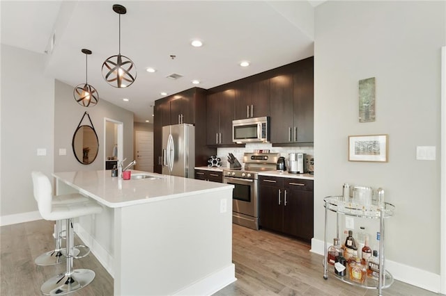 kitchen with sink, decorative light fixtures, a kitchen bar, a center island with sink, and appliances with stainless steel finishes