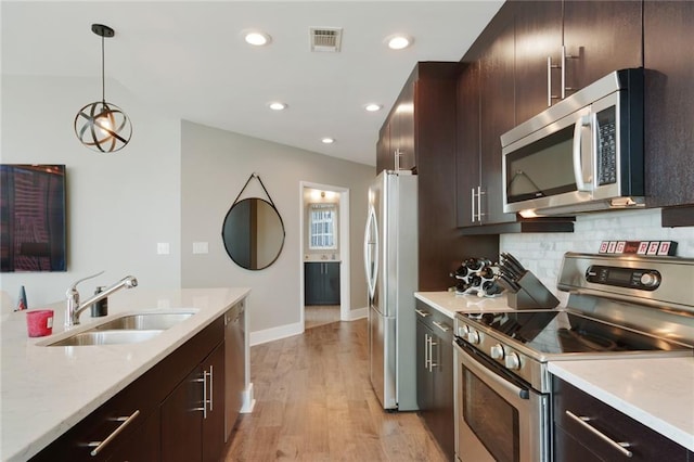 kitchen with decorative backsplash, appliances with stainless steel finishes, sink, decorative light fixtures, and light hardwood / wood-style flooring