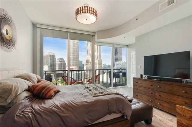 bedroom with access to outside, a wall of windows, and light hardwood / wood-style floors