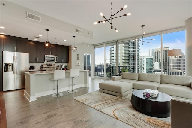 living room with light hardwood / wood-style floors, a wall of windows, a healthy amount of sunlight, and a notable chandelier