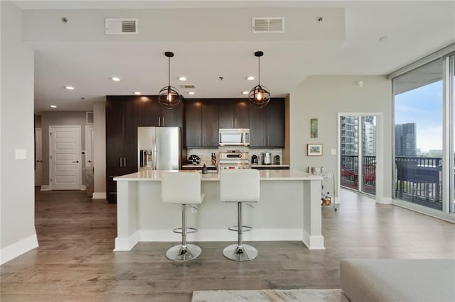 kitchen with a center island with sink, appliances with stainless steel finishes, tasteful backsplash, decorative light fixtures, and a breakfast bar area