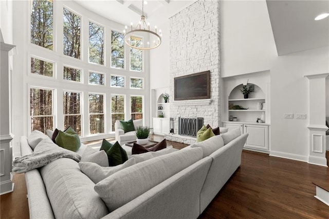 living room featuring baseboards, dark wood-type flooring, built in shelves, a chandelier, and a fireplace