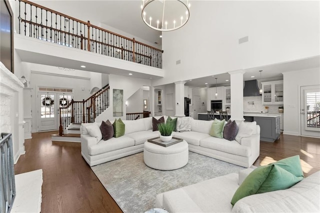 living room with a chandelier, stairway, ornate columns, and wood finished floors