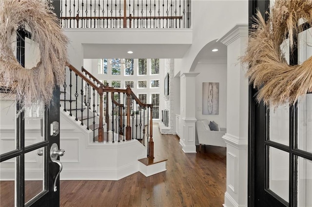 foyer featuring a towering ceiling, ornate columns, stairs, and wood finished floors