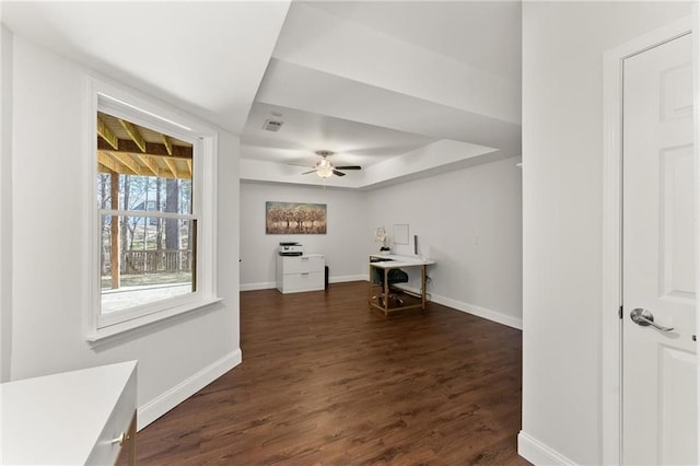 office with dark wood-style floors, visible vents, baseboards, and a tray ceiling