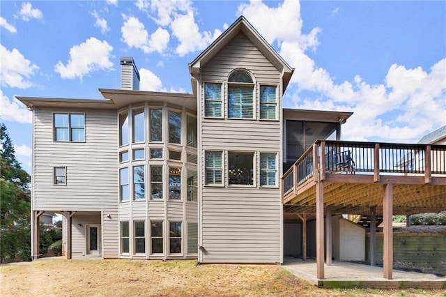 back of house featuring a sunroom, a patio area, a chimney, and a wooden deck