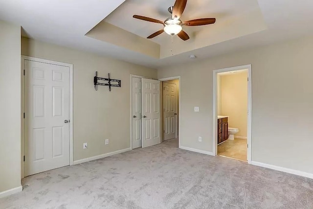 unfurnished bedroom with light carpet, a tray ceiling, ceiling fan, and ensuite bathroom