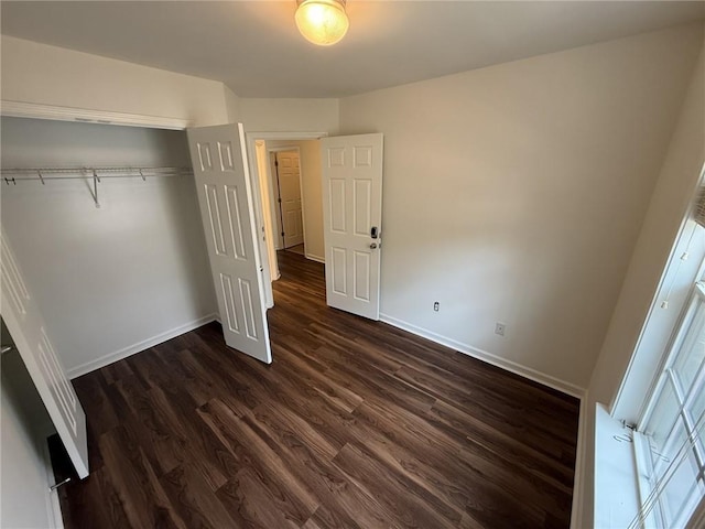 unfurnished bedroom with dark wood-style floors, a closet, and baseboards