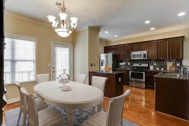 dining space with sink, light hardwood / wood-style flooring, ornamental molding, and a chandelier