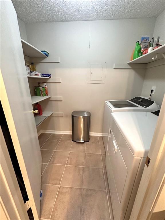 clothes washing area with light tile patterned floors, a textured ceiling, and washing machine and clothes dryer