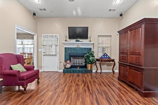 living room with a textured ceiling, dark hardwood / wood-style floors, and a tiled fireplace