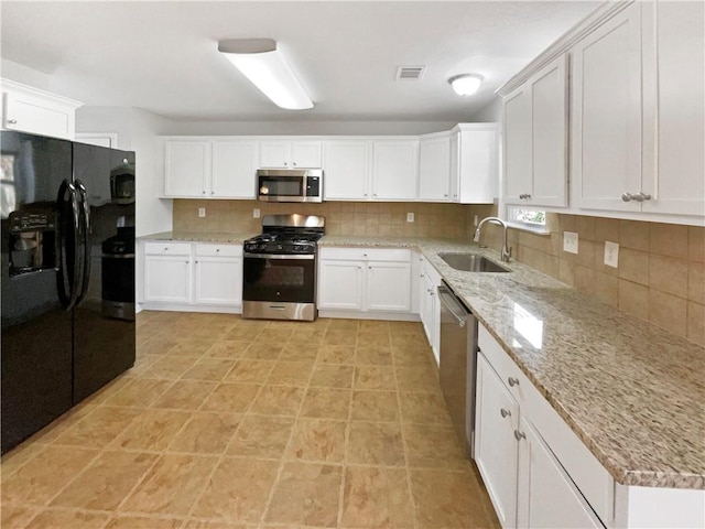 kitchen with white cabinets, sink, light stone countertops, appliances with stainless steel finishes, and tasteful backsplash