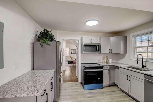 kitchen featuring light stone counters, gray cabinets, stainless steel appliances, light hardwood / wood-style flooring, and sink