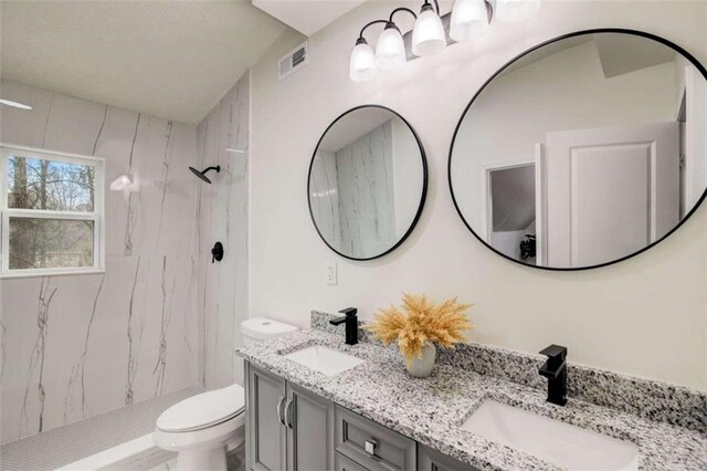 bathroom with a tile shower, vanity, and toilet