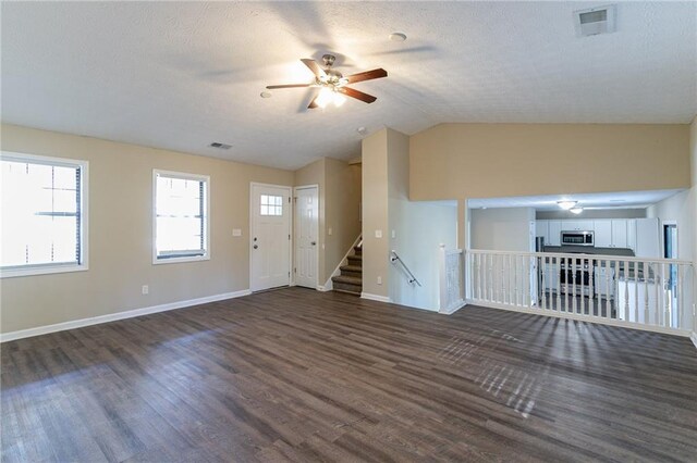 unfurnished living room featuring a textured ceiling, ceiling fan, dark wood-type flooring, and vaulted ceiling