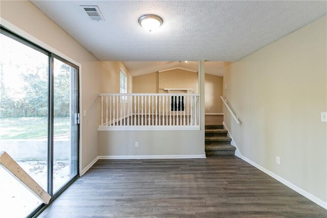 empty room with a textured ceiling, dark wood-type flooring, and lofted ceiling