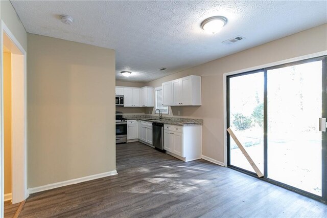 kitchen with white cabinets, a textured ceiling, stainless steel appliances, and dark wood-type flooring