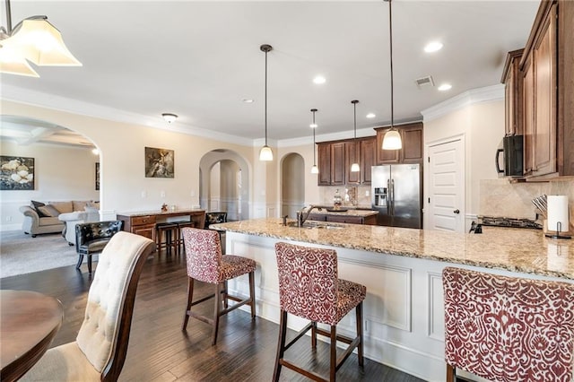 kitchen featuring black microwave, arched walkways, stainless steel fridge, and a sink