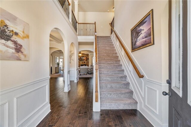 stairway featuring hardwood / wood-style floors, a wainscoted wall, arched walkways, a decorative wall, and a high ceiling