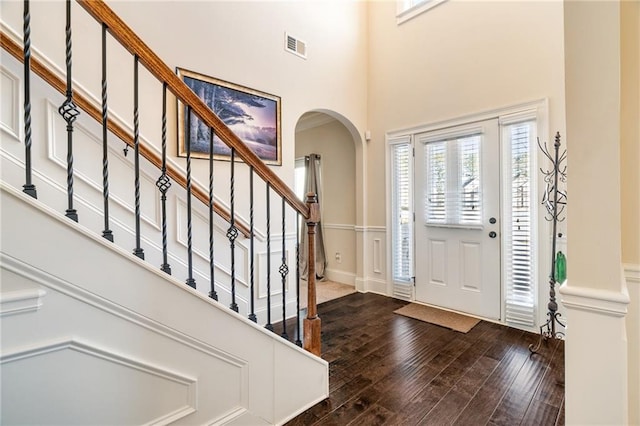 foyer entrance featuring visible vents, arched walkways, a high ceiling, and dark wood-type flooring