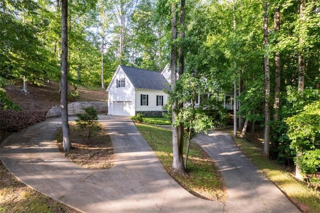 view of front of property featuring an attached garage, driveway, view of scattered trees, and an outdoor structure