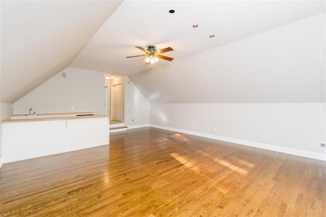 additional living space featuring light wood-style floors, ceiling fan, lofted ceiling, a sink, and baseboards