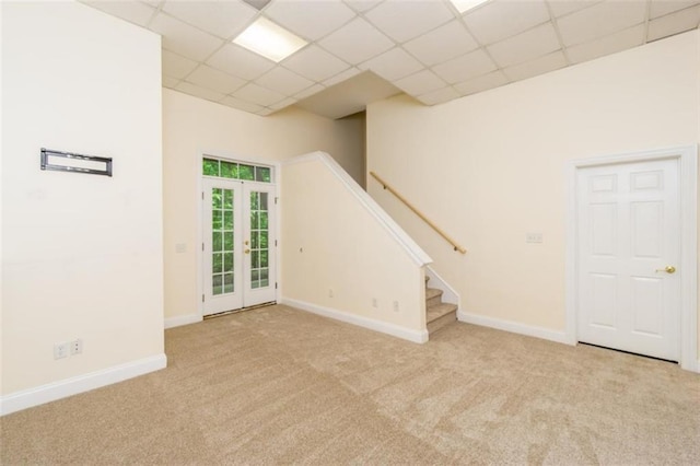 unfurnished room featuring a paneled ceiling, carpet, baseboards, stairs, and french doors