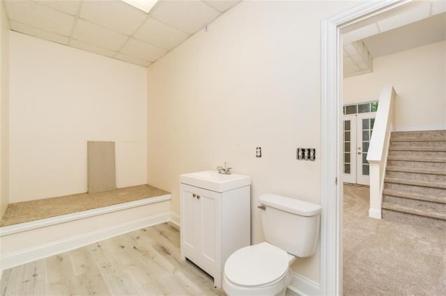 bathroom featuring a drop ceiling, toilet, baseboards, wood finished floors, and vanity