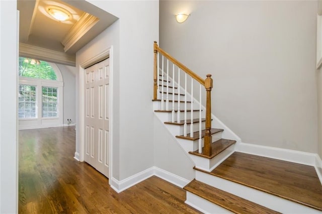 staircase with wood finished floors, ornamental molding, and baseboards