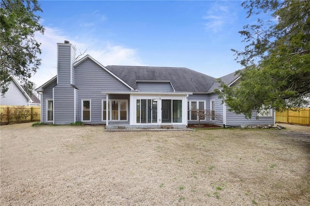 back of house with a lawn, a chimney, fence, and a sunroom